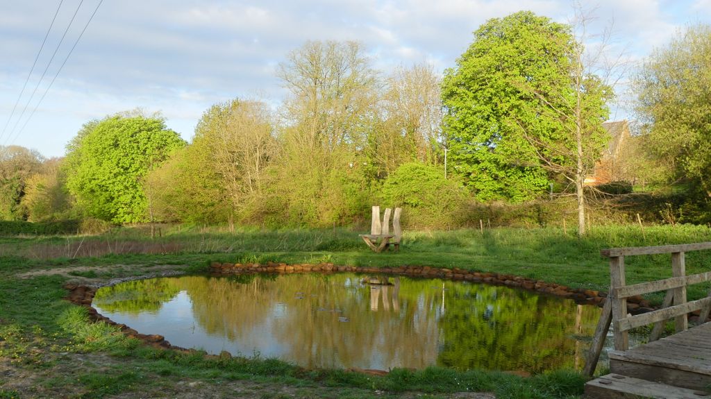 New pond with stone edging and still water, with grass and trees in Spring
